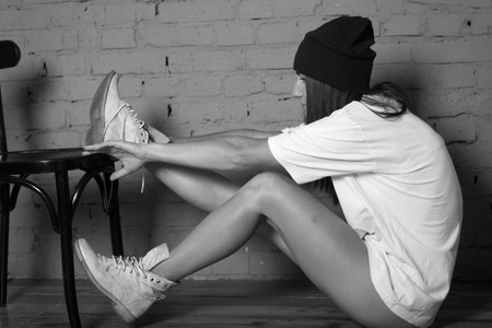 Girl in a white t-shirt and a black hat fashion style clothing feelings against a brick wallの写真素材