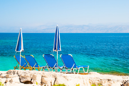 Blue sunbeds and blue-white parasols (umbrellas) on a beautiful rock beach.の写真素材