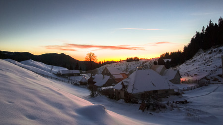 Winter sunset over village of Fundata. Mountain landscape with houses covered by snow in Carpathian Mountains, Romaniaの写真素材