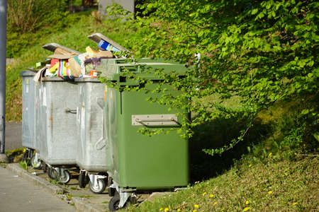A green plastic container for organic waste, behind it metal containers for cardboard overfilledのeditorial素材