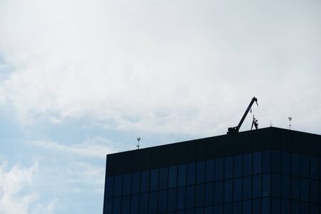 A rooftop of a corporate building. On it there are crane and other construction machinery in order to repair the terraced roof. The whole scene is seen in silhouettes due to light conditions.の写真素材
