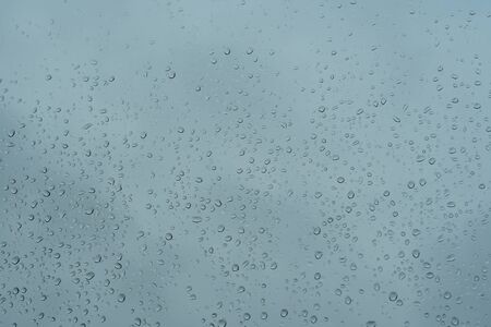 Rain drops sticking on the window pane in heavy downpour with cloudy sky on the backgroundの写真素材