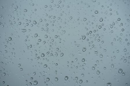 Rain drops close-up sticking on the window pane in heavy downpour with cloudy sky on the background