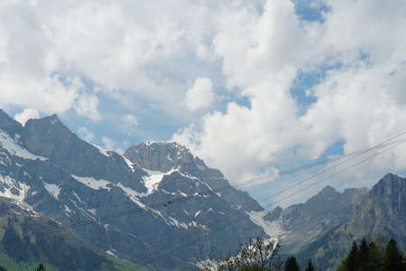 Alpine landscape In the springtime with hills covered by coniferous woods and mountains covered with...