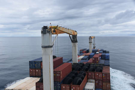 Le Havre / France - 05 23 2020: Merchant cargo container vessel with cranes underway through calm Atlantic ocean under overcast sky. Ship carries with closed and open top containers loaded with tires.のeditorial素材
