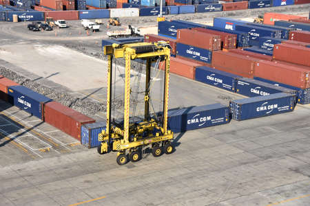 A straddle carrier in Kingston Freeport Terminal passing near containers. Yellow straddle truck is...