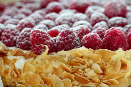 A cake thickly covered with raspberries decorated with powder sugar. The side is covered with custard and roasted almond flakes or slices. Close up view of a dessert.の写真素材