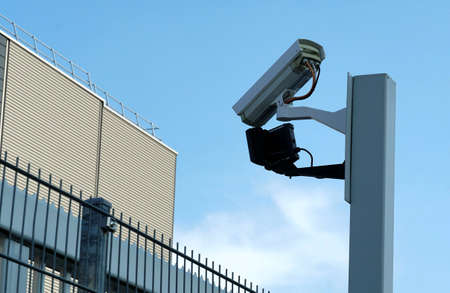 CCTV security camera on a post to watch factory yard of private company for security reasons with blue sky as background. In general serves as a symbol for control, observation spying and protection.の写真素材