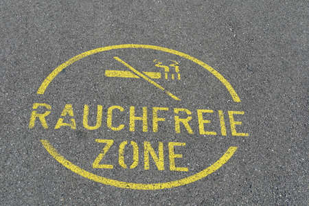 A round sign for a smoke free zone on the street or asphalt road written in German language  with a picture of a stroked out or cancelled cigarette. The sign is painted in yellow color.の写真素材