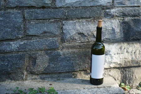 An empty wine bottle of a dark glass with a white label and a cow stopper standing on the street against a stone wall. A photo with a lot of copy space.の写真素材