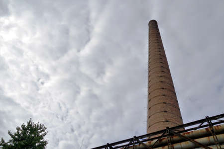 Tall brick chimney photographed at low angle in an old industrial zone in a provincial town in Eastern Europe. The chimney is out of service, it is only remnant of former activity in heavy industry.の写真素材