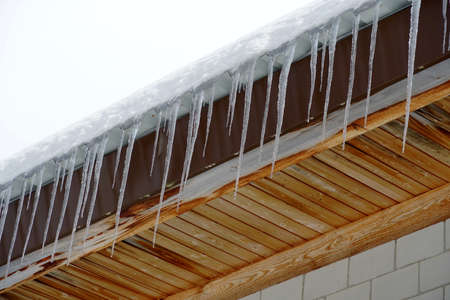 Rooftop with melting icicles hanging dome with drops of water falling down on the background of blue...