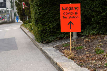 Test station Covid-19 signpost in German in orange color showing with arrow the direction to the testing center on the ground of Zurich University Hospital in Switzerland. It is beside sidewalk.のeditorial素材