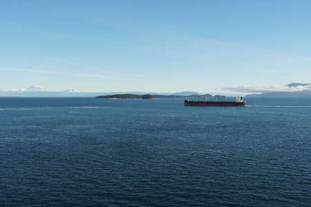 View form the container ship on another cargo ship with mountain covered with snow in background during approaching to Vancouver, British Columbia, from Pacific ocean.の写真素材