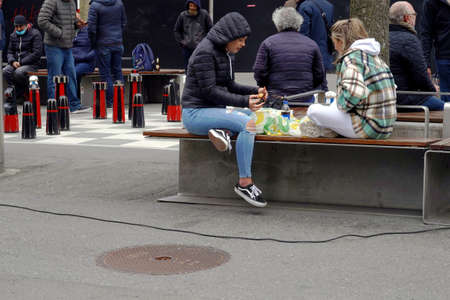 Bern, Switzerland - 04 03 2021: Street life in the city, in time of coronavirus and covid-19 crisis. People sit around, eat take away food, play chess and some of them wear face masks.のeditorial素材