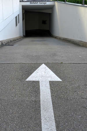 Entrance to an underground parking with a white arrow showing direction. Above the entrance is...