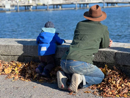 Father and his toddler son lean on concrete barrier and observe lake Zurich in Switzerland. Rear view with water on the background.の写真素材