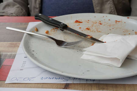 White empty plate with bread crumbs of pizza. On shallow plate is cutlery as knife and fork and...