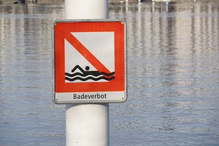 Square shaped signpost saying in German bathing prohibited attached on a metal pole. Placed in Lake Lucerne in Switzerland. The lake itself is on the background. It is warning symbol against danger.の写真素材