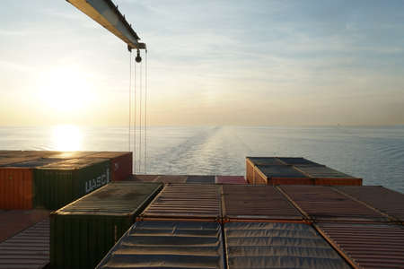 Venice, Italy - 05 13 2022: Sunset observed behind the container vessel with crane from navigational bridge sailing through Mediterranean Sea. In horizon is keel water and orange, blue sky with cloudsのeditorial素材