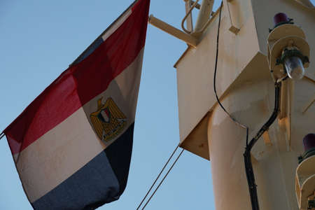 Egypt flag is fluttering on the mast of merchant container ship moored in port of Damietta. In background is also visible blue sky.のeditorial素材