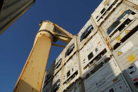 Koper, Slovenia - 05 07 2022: Cream color cargo crane between white reefers containers lashed and...