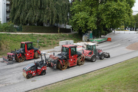 Red asphalt paving machines such as street rollers and wheel dozer are parked on the street ready...