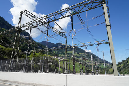 Behind fence is high voltage electricity power distribution plant with cables, expulsion fuses, surge arrester and other components as a  part of hydroelectric power plant.の写真素材