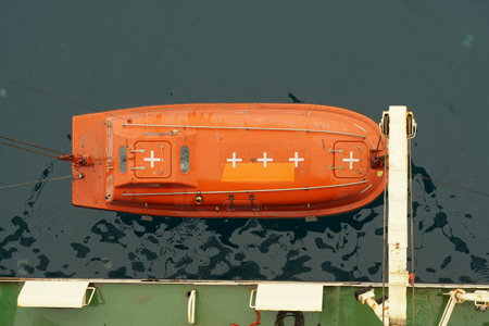 Top view on the orange colour life boat with reflective tape stickers secured with davits and safety hooks on the merchant cargo container vessel sailing through Adriatic Sea.の写真素材