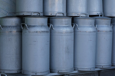 Milk churns made of metal stacked in rows. They have two handles and a cover. Cutout of stored churns  suitable as background with agriculture, food or dairy themes.の写真素材