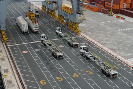 Tracks or lorries in lines with numbers are waiting below gantry cranes for loading containers from...