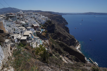 A view of blue and white terraced houses of Santorini from the town of Fira at the top of the mountain. To the right is the azure blue sea and the mountain massif forming island.の写真素材