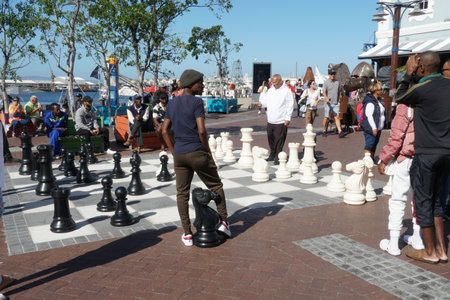 Local players of street chess enjoy a game  with giant chess men on the Waterfront in Cape Town South Africa. Some other visitors standing and observing.のeditorial素材