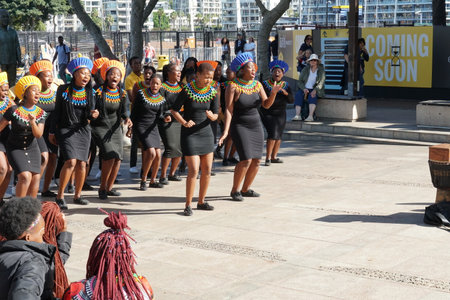Street singing and dancing group of African women in traditional dresses entertains tourist passing by in waterfront district in Cape Town during sunny summer day.のeditorial素材