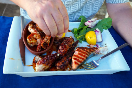 A hand is seasoning a dish of sea fruits and grilled fish served on a square white plate. The hand...
