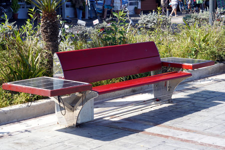A red wooden bench outfitted with solar photovoltaic panels for mobile phone charging and serving as a component of a smart city project.の写真素材