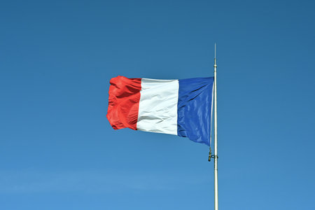 French flag hoisted on a flagpole waving in the wind. Low angle view against blue sky with plenty of copy space.の写真素材