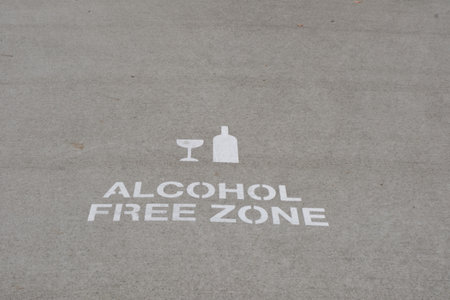 A sign for alcohol free zone on the street or asphalt road written in Nelson, New Zealand with a picture of glass and bottles. The sign is painted in white color.の写真素材
