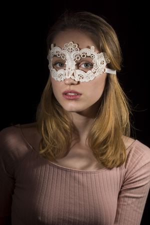 Teenage girl wearing lace mask on black backgroundの写真素材