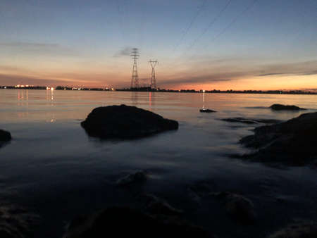 Power line in the sea at sunset. High-voltage pylons.の写真素材