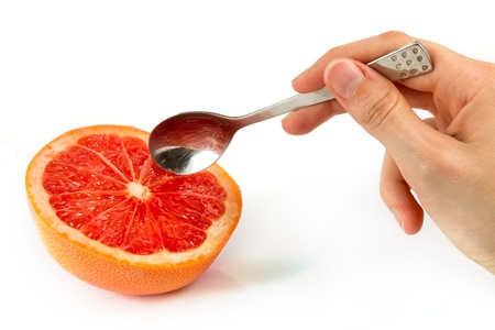 Pink grapefruit with hand holding a spoon on whiteの写真素材