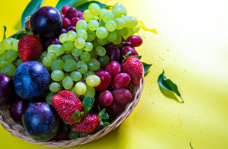 Grapes and plums in a basket on a yellow background