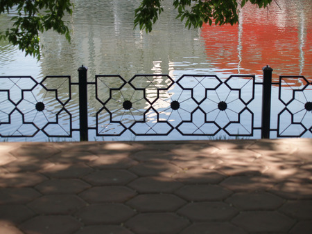 Summer Trees and iron fence near urban pond with red reflecshionsの写真素材