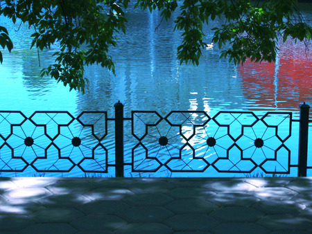 Summer Trees and iron fence near urban pondの写真素材