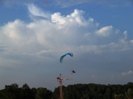 Paraglider against cloudy sky and construction craneの写真素材
