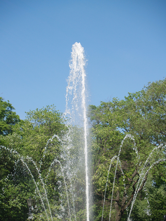 The fountain streams against blue sky and sunner foliageの写真素材