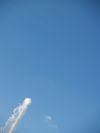 The top of fountain stream against blue sky with small cloudの写真素材