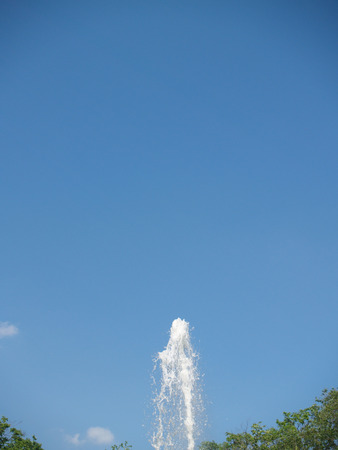 The fountain streams against blue sky and sunner foliageの写真素材