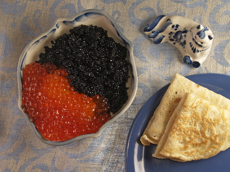 black and red caviar in a traditional porcelain  blue and white dishes and a toy cat and pancakesの写真素材