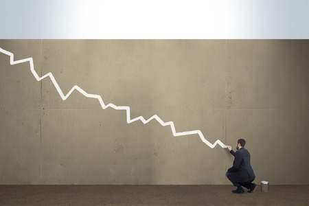 A business man draws a falling chart on a concrete barrier.の写真素材